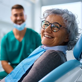 Woman with black glasses smiling while sitting in the dental treatment chair