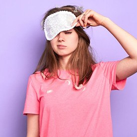 Woman sleepily pulling a night mask off her face