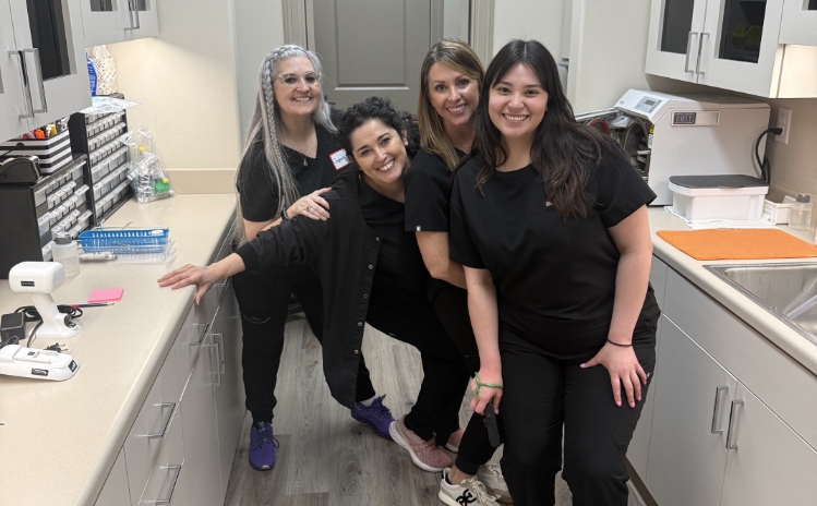 Three dental team members smiling together in a treatment room