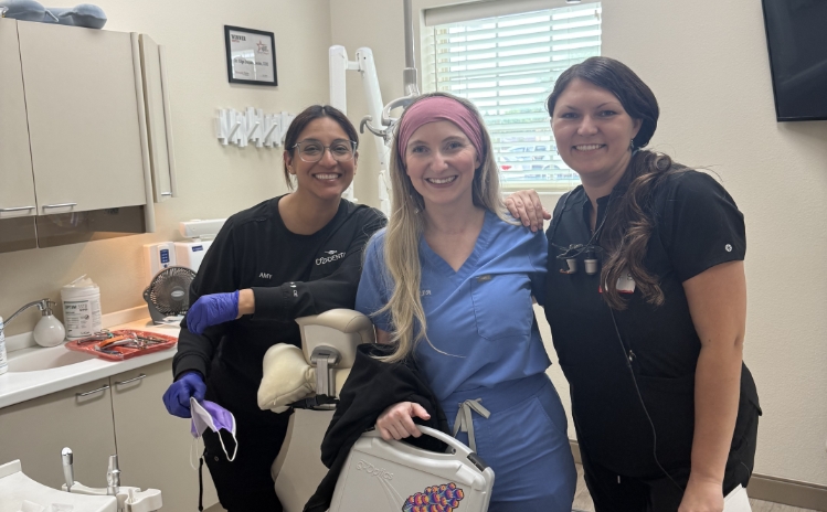 Dentist and assistant smiling next to a patient in a dental chair