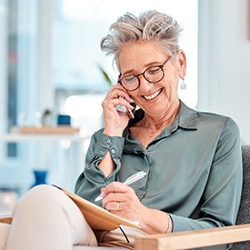 Woman with green shirt and gray hair sitting in chair talking on smartphone