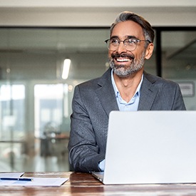 Man with silver hair in business attire and glasses working on laptop
