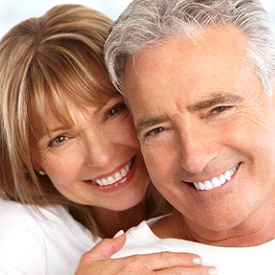 An older couple smiling and hugging after receiving their metal-free restorations in Mesquite