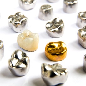 A metal-free dental crown sitting among various silver and gold crowns in Mesquite