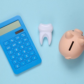 Calculator, tooth, and piggybank arranged against blue background