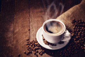 Steaming cup of coffee with coffee beans nearby on table.